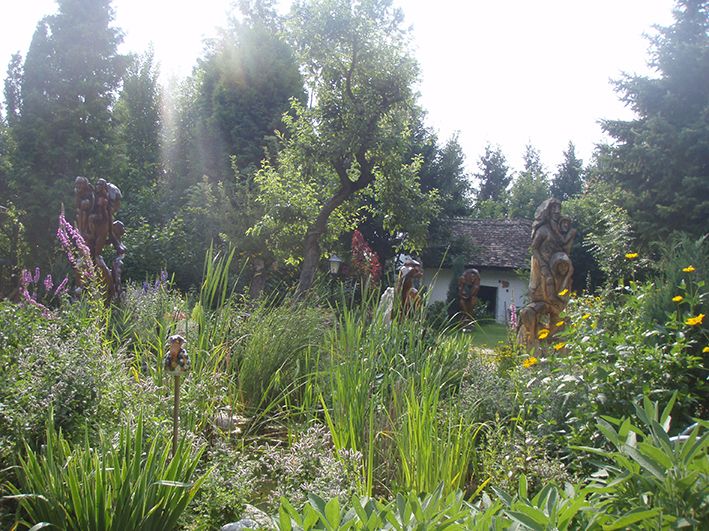 A lush garden with sculptures, trees and a small building in the background.
