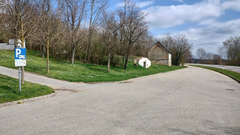 Parkplatz mit Wohnmobilstellplatzschild, Bäume und altes Gebäude im Hintergrund.