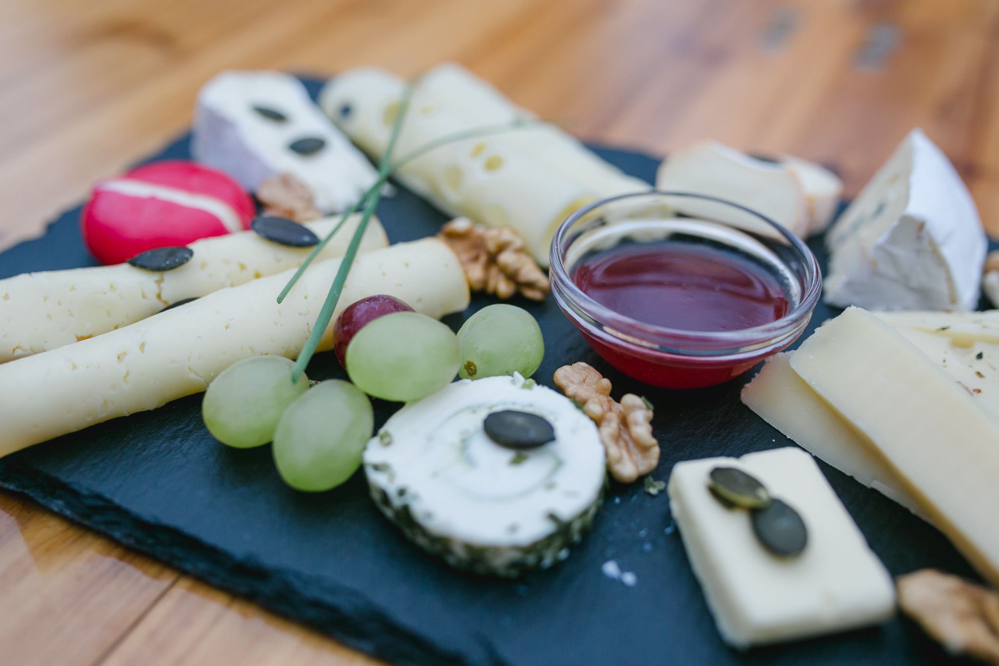 Käseplatte mit Trauben, Nüssen und Dip auf Schieferplatte.