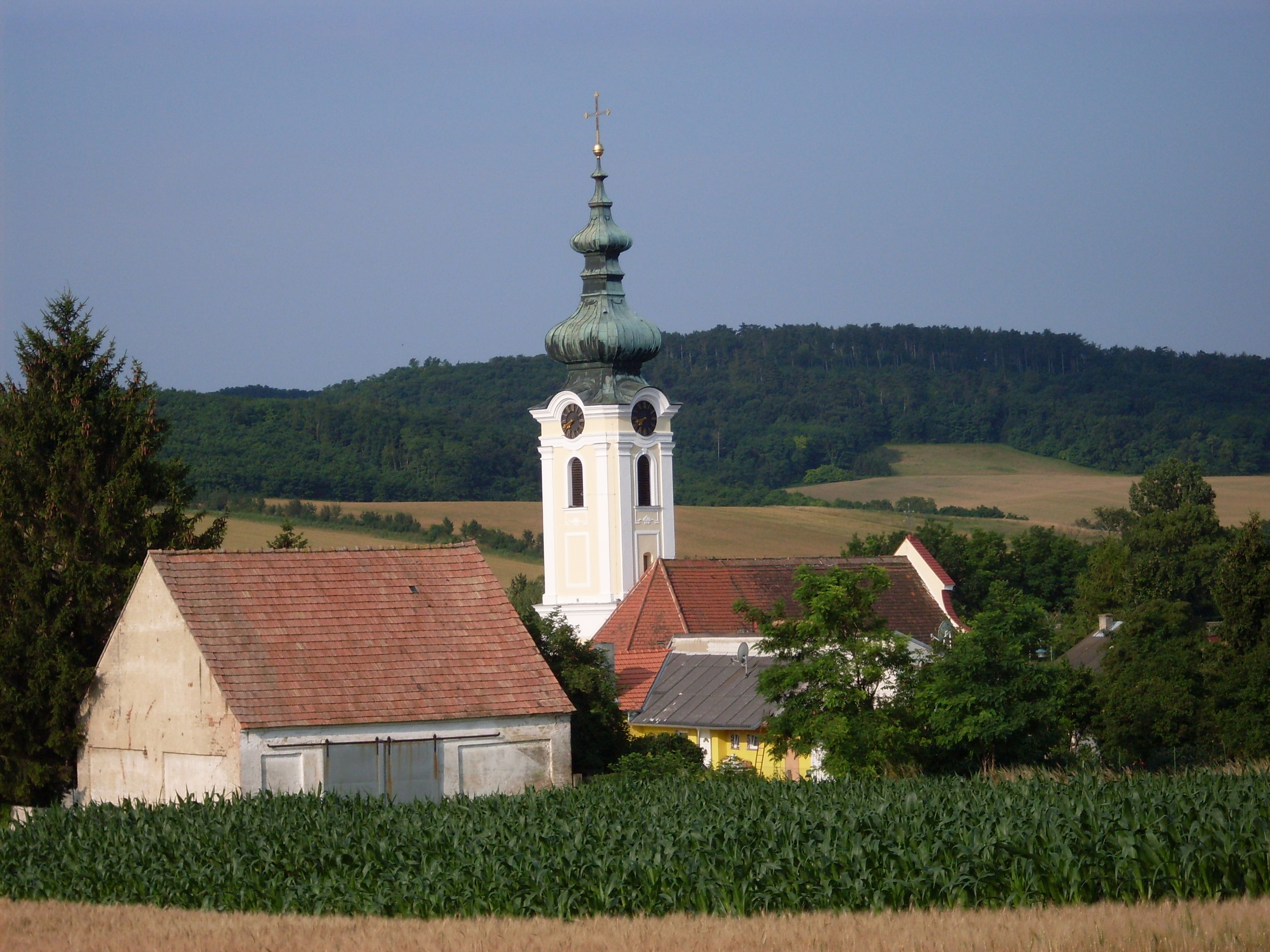 Eine Kirche mit Zwiebelturm in einer ländlichen Umgebung, umgeben von Feldern und Bäumen.