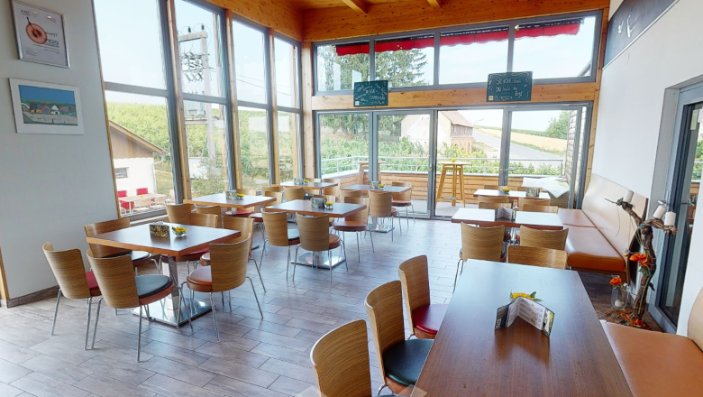 Innenansicht eines modernen Heurigen mit Holzmöbeln und großen Fenstern.