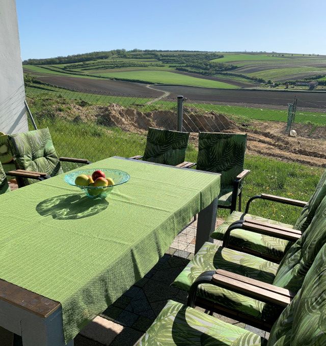 Terrasse mit grünem Tisch und Stühlen, Blick auf Felder und Hügel.