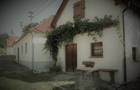 Ein traditionelles weißes Gebäude mit roten Ziegeldach und Efeu an der Fassade. Im Vordergrund steht ein alter Brunnen.