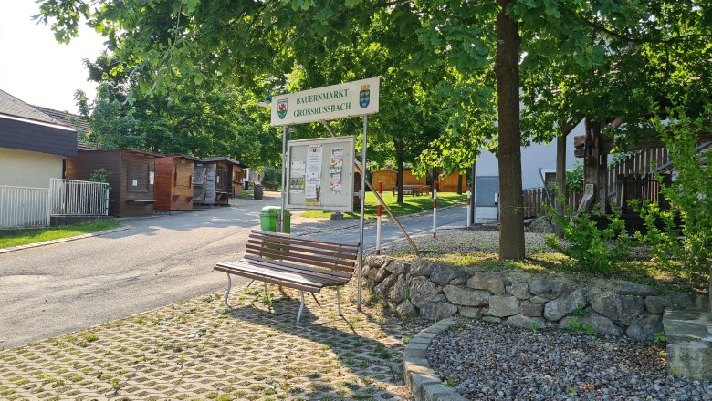 Eingang zum Bauernmarkt Großrußbach mit Holzhütten und Bänken.