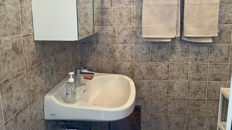 Ein Badezimmer mit Waschbecken, Spiegel, Handtüchern und Fliesen.