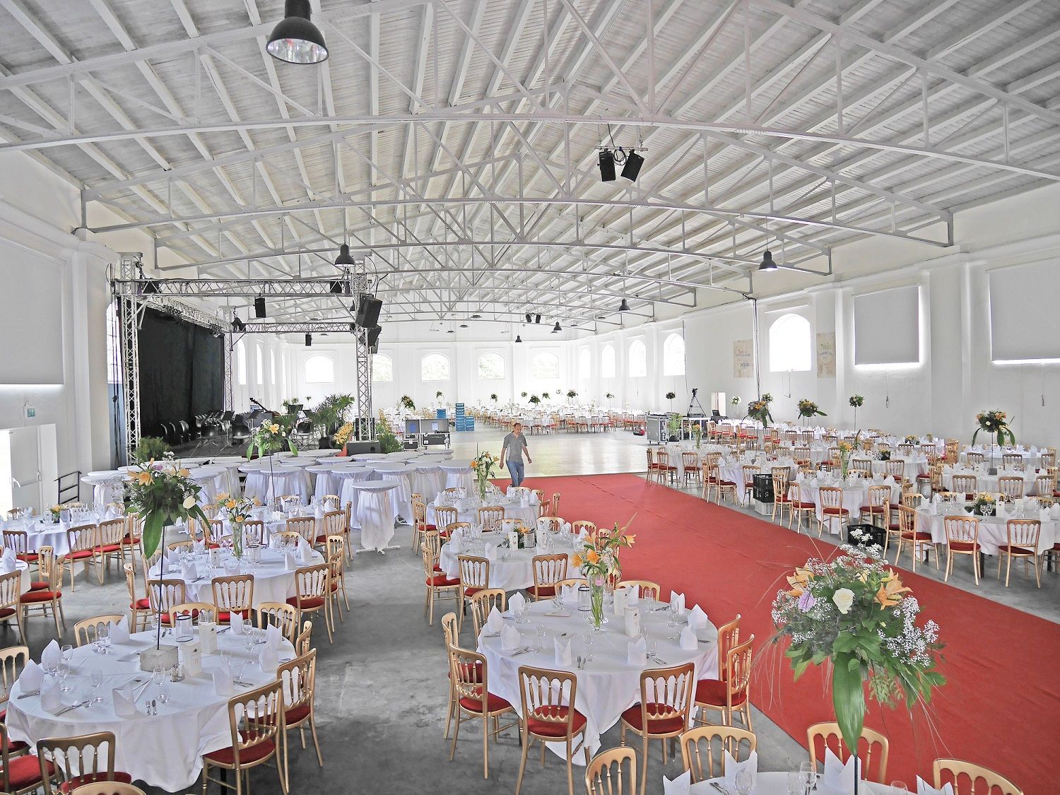 Interior view of a large hall with gala seating, round tables and a stage.