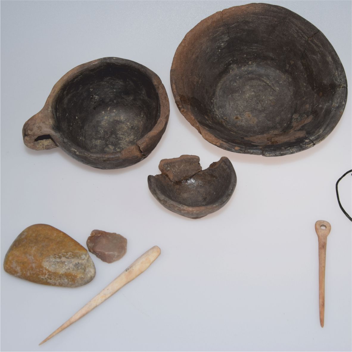 Prehistorické artefakty, jako jsou mísy, nástroje a kameny, na bílém pozadí.