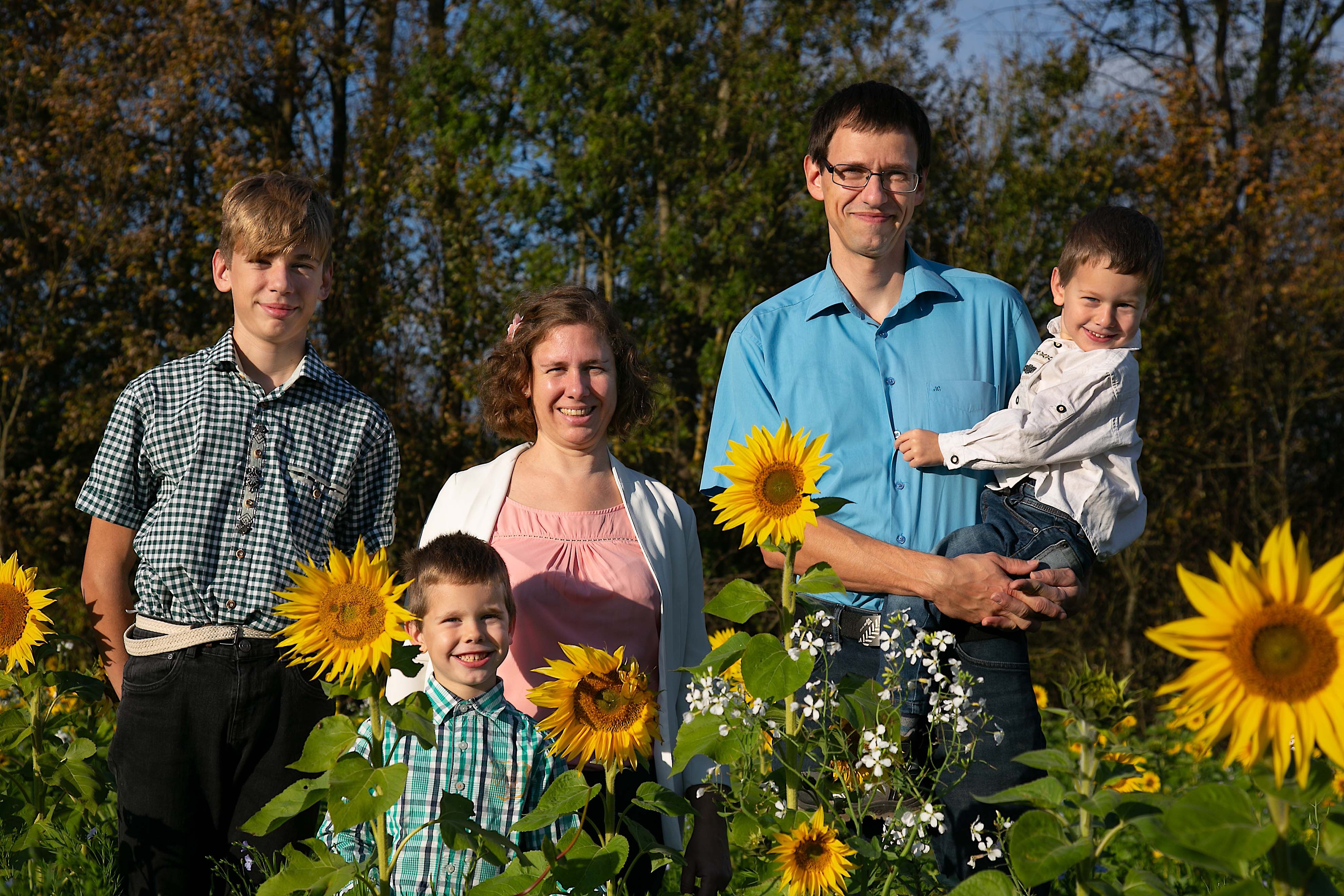 Eine Familie steht lächelnd in einem Sonnenblumenfeld.