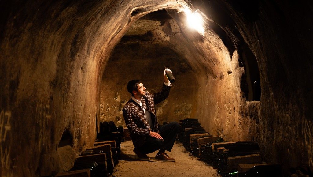 A man in a wine cellar holds a bottle up to the light.