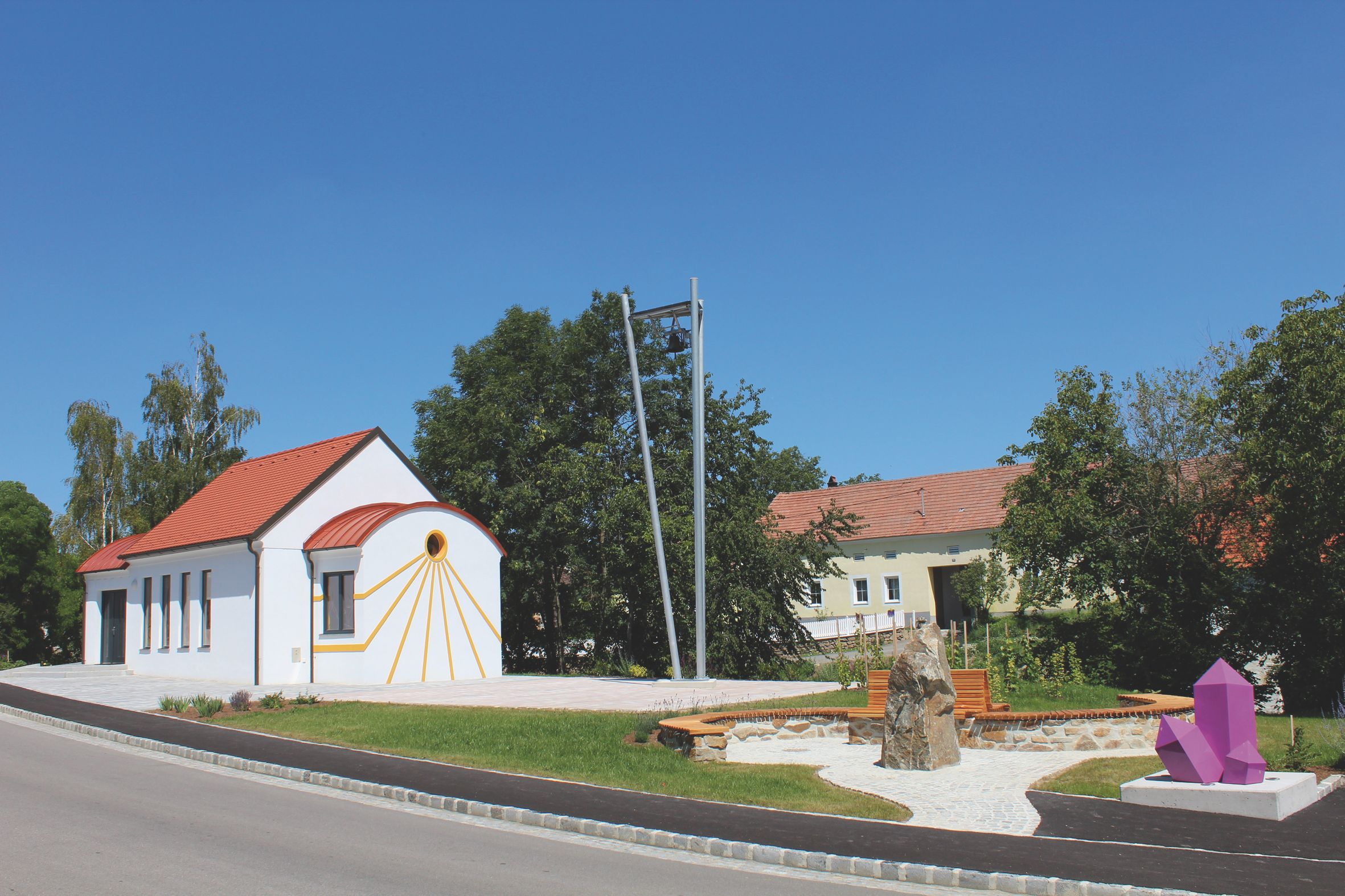 Weiße Kapelle mit rotem Dach und Amethystskulptur im Vordergrund.