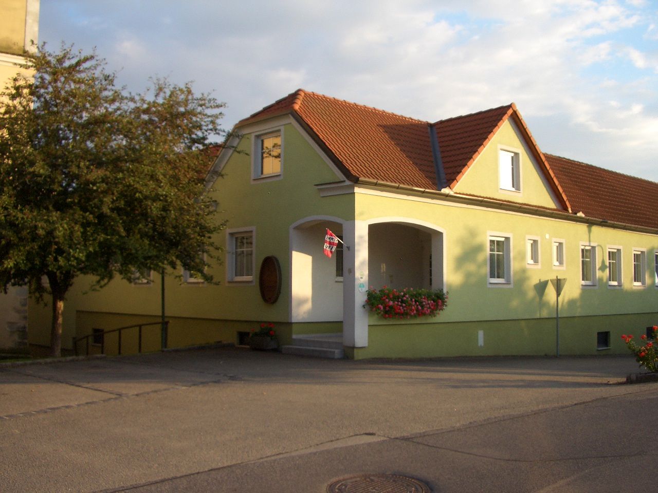 Gelbes Gebäude mit rotem Dach und Blumen am Eingang.