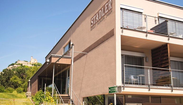 Modernes Gebäude des Weinguts Stadler mit Terrasse und Burg im Hintergrund.