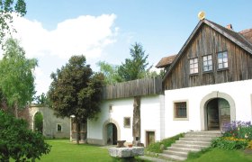 Ein traditionelles Gebäude mit Holzdach und weißer Fassade, umgeben von einem grünen Garten.