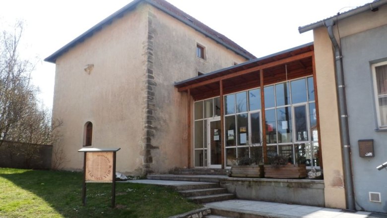 Ein historisches Gebäude mit modernem Anbau und einem Schild im Vordergrund.