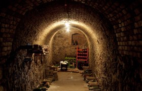 Ein schmaler, gewölbter Weinkeller mit Ziegelwänden und gelagerten Flaschen.