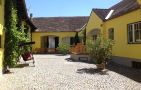 Innenhof eines gelben Winzerhofs mit Pflastersteinen, Schaukel und Pflanzen.