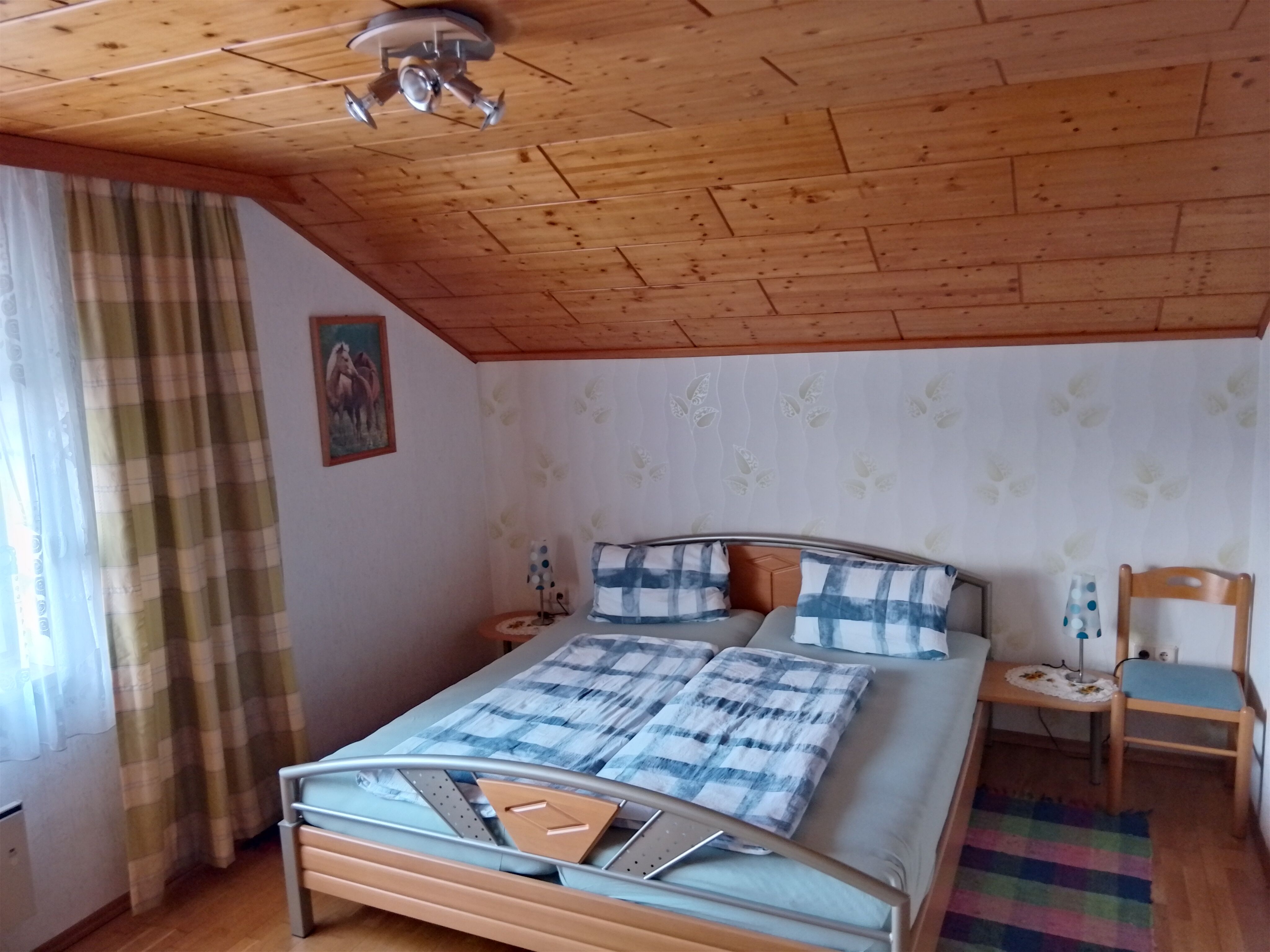 Gemütliches Schlafzimmer mit Doppelbett, Holzdecke und gemusterten Vorhängen.
