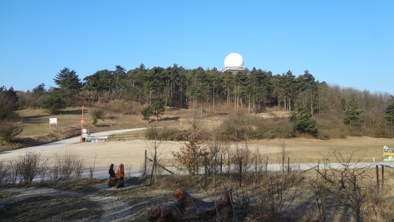 Landschaft mit Hügel, Wald und Radarkuppel unter blauem Himmel.