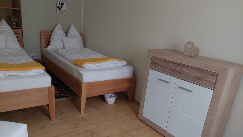 Zweibettzimmer mit zwei Einzelbetten, Holzboden und Kommode.