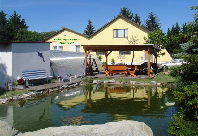 Au&szlig;enansicht einer gelben G&auml;stepension mit Teich und Pavillon.