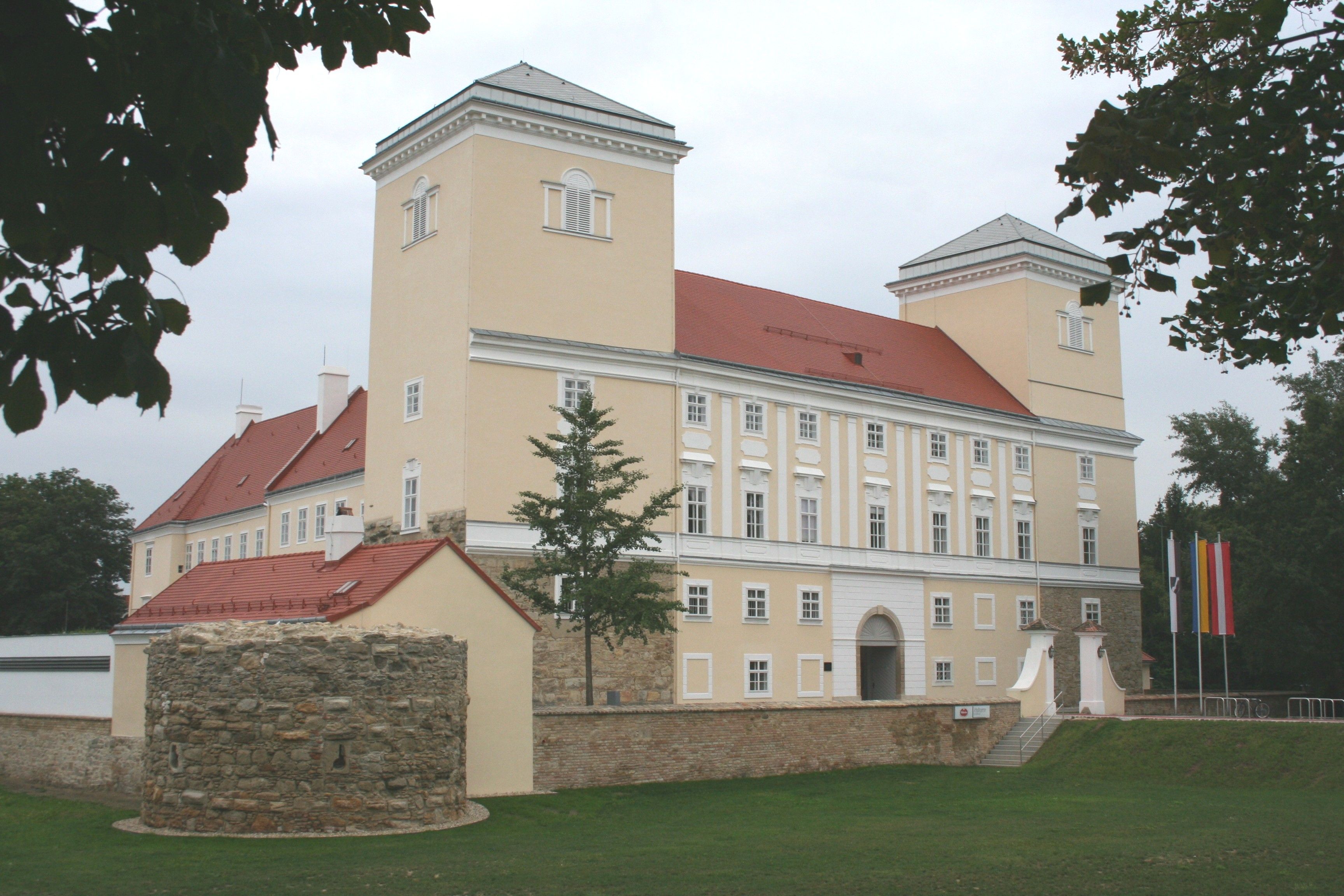 Schloss Wolkersdorf mit zwei Türmen und einem runden Steinturm im Vordergrund.