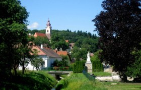 Landschaft mit Kirche und Statue in einem Dorf.