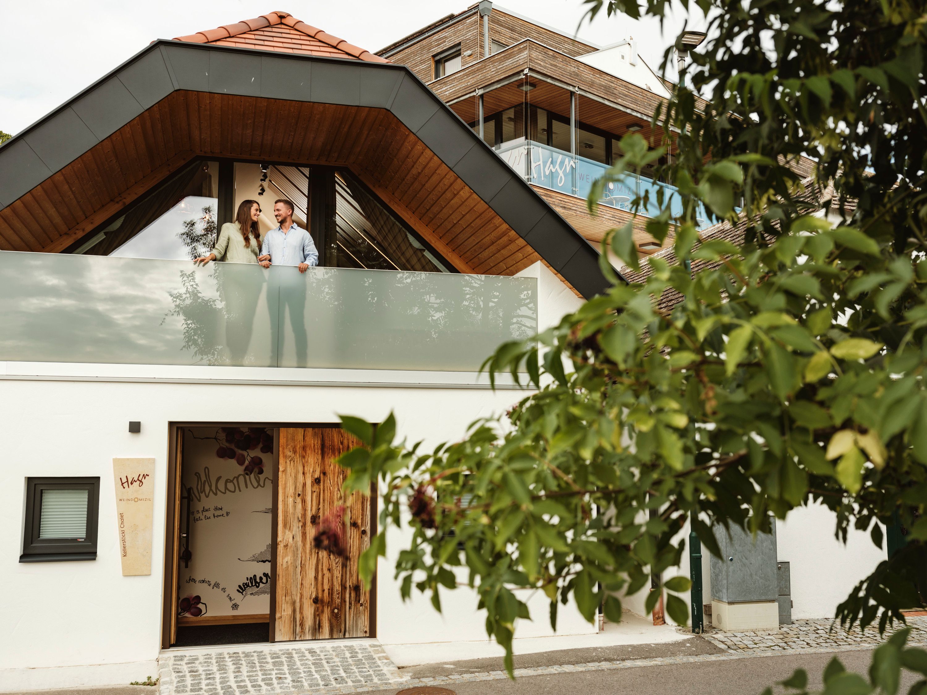 Ein modernes Gebäude mit einem Paar auf dem Balkon, umgeben von Bäumen.