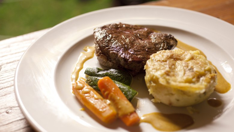 Ein Teller mit einem Stück Fleisch, Gemüse und einer Kartoffelbeilage.