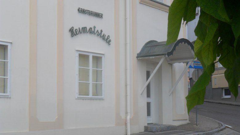 Eingang zur Ernstbrunner Heimatstube mit Vordach und Straßenschild.