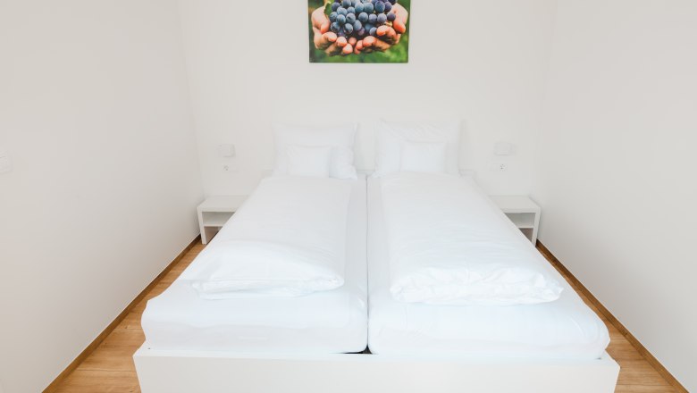 Ein schlichtes, modernes Schlafzimmer mit einem Doppelbett und einem Bild von Trauben an der Wand.