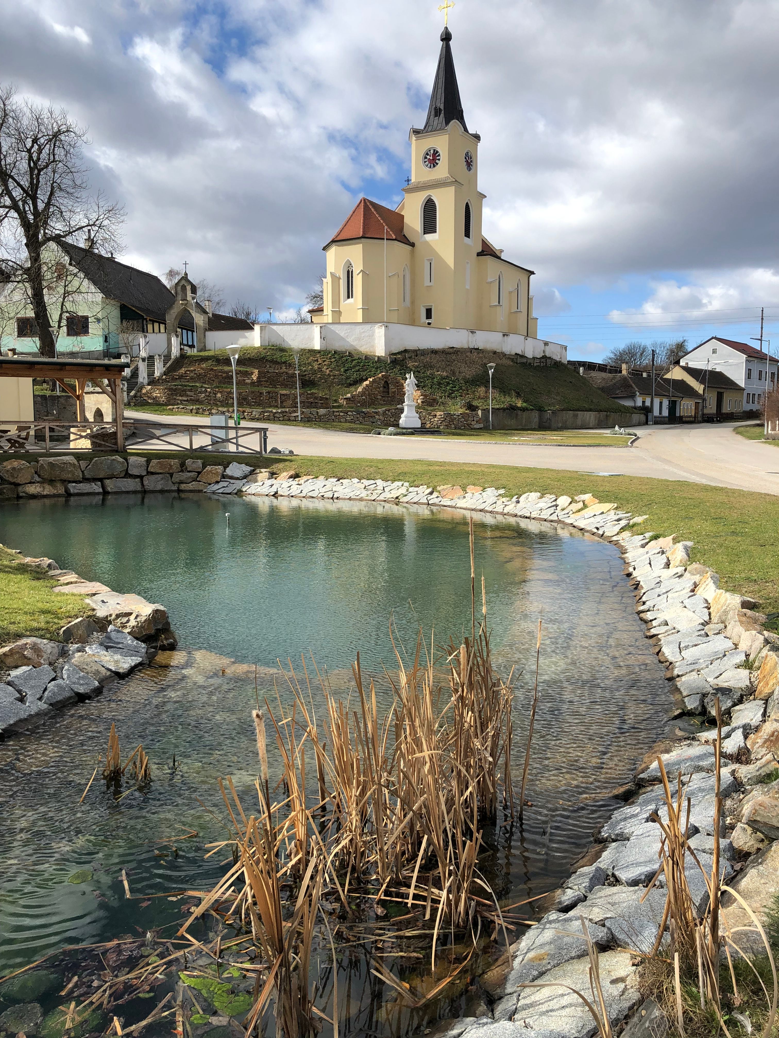 Kirche in Glaubendorf mit Teich im Vordergrund.
