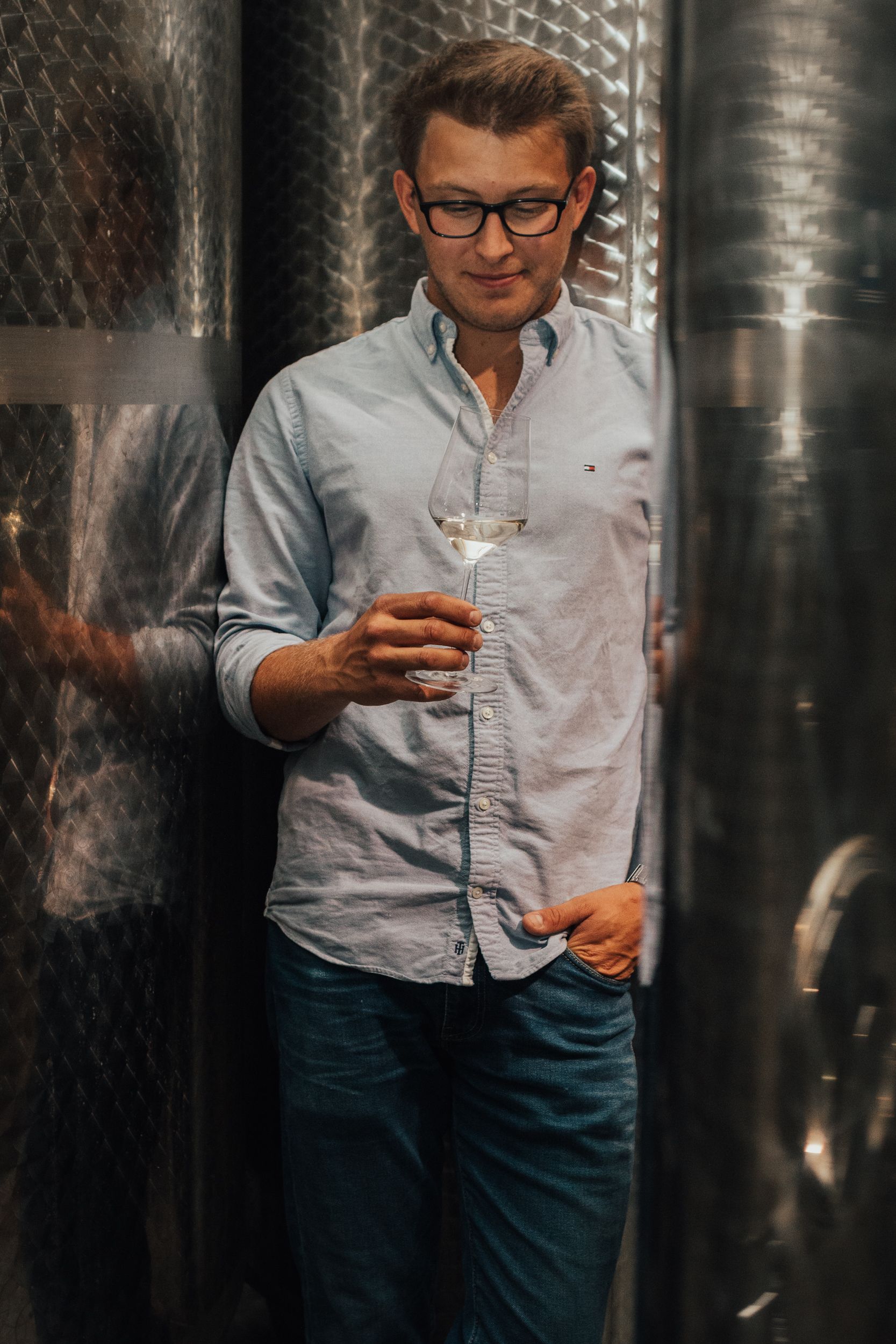 Mann mit Brille hält ein Weinglas in einem Weinkeller.