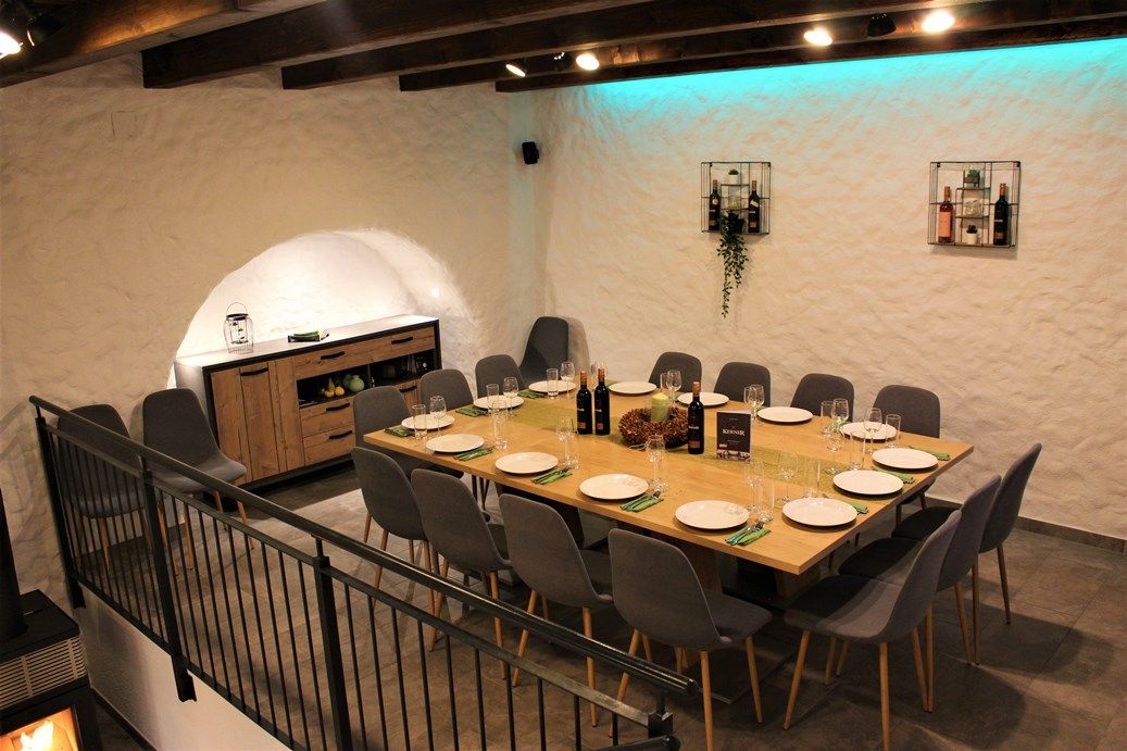 Ein stilvoll gedeckter Tisch in einem Weinkeller mit modernen grauen Stühlen und dekorativer Beleuchtung.