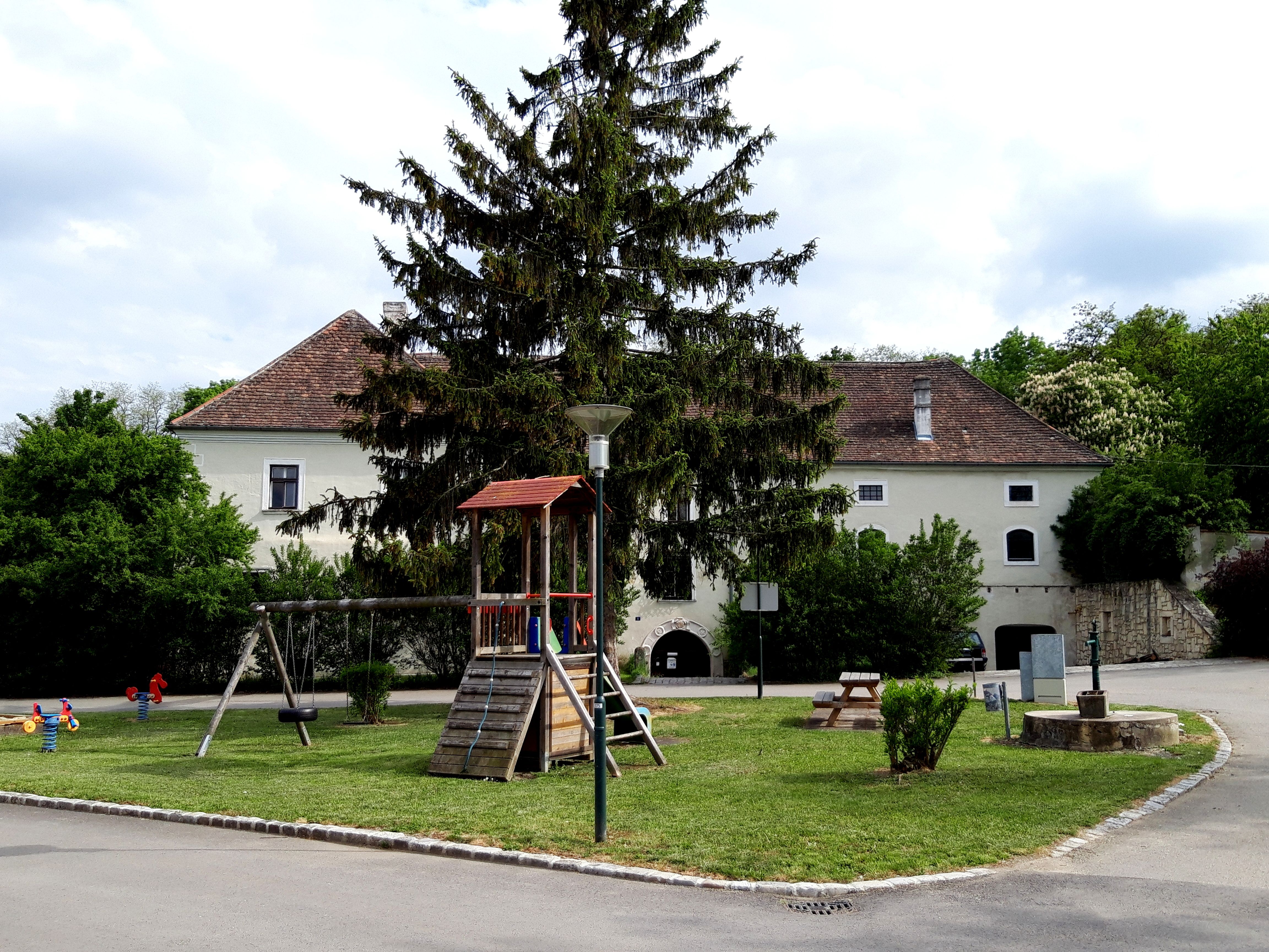 Spielplatz mit Klettergerüst und Schaukel vor einem historischen Gebäude in Zellerndorf.
