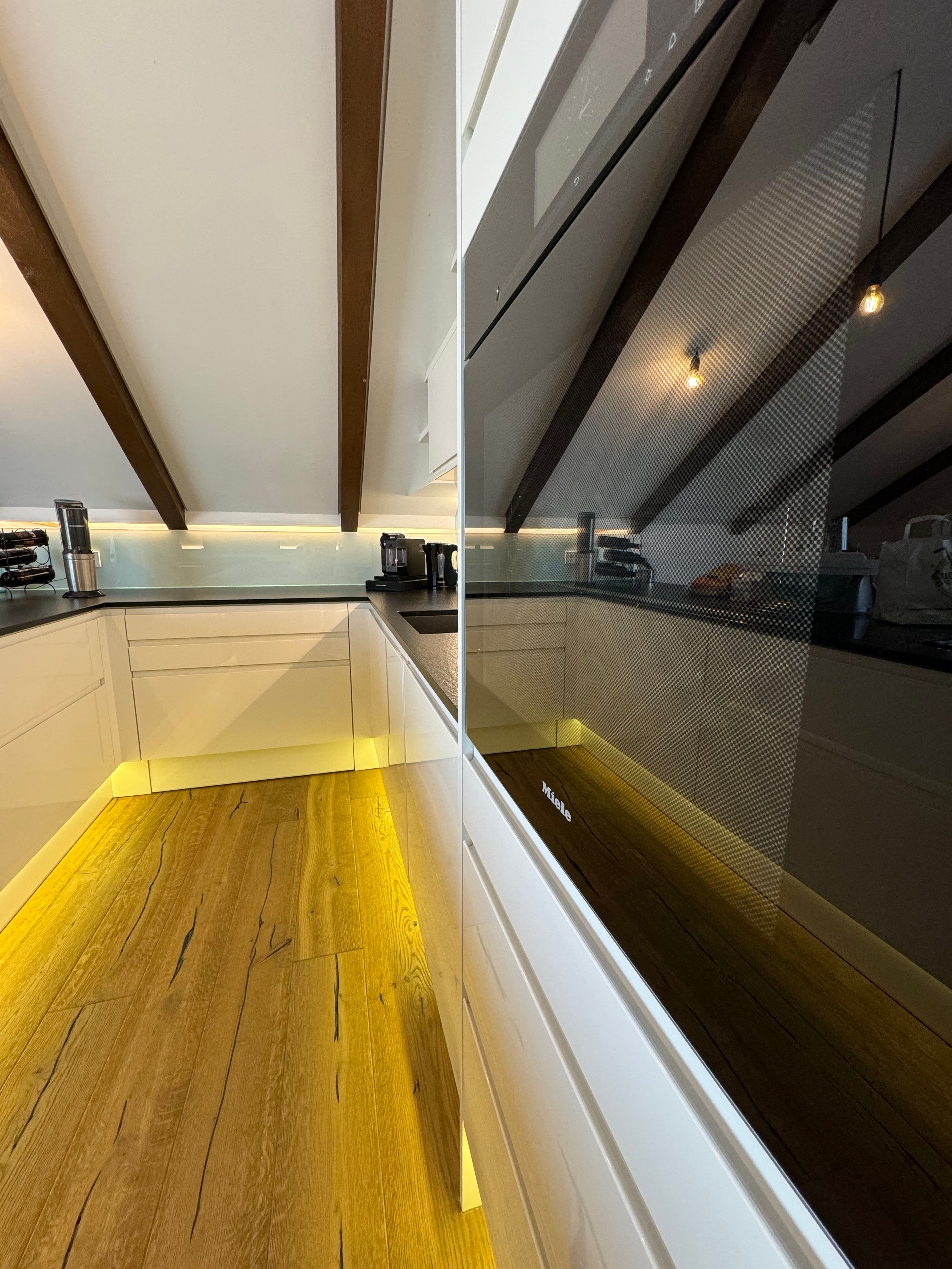 Moderne Küche mit Holzfußboden, weißen Schränken und eingebautem Ofen.