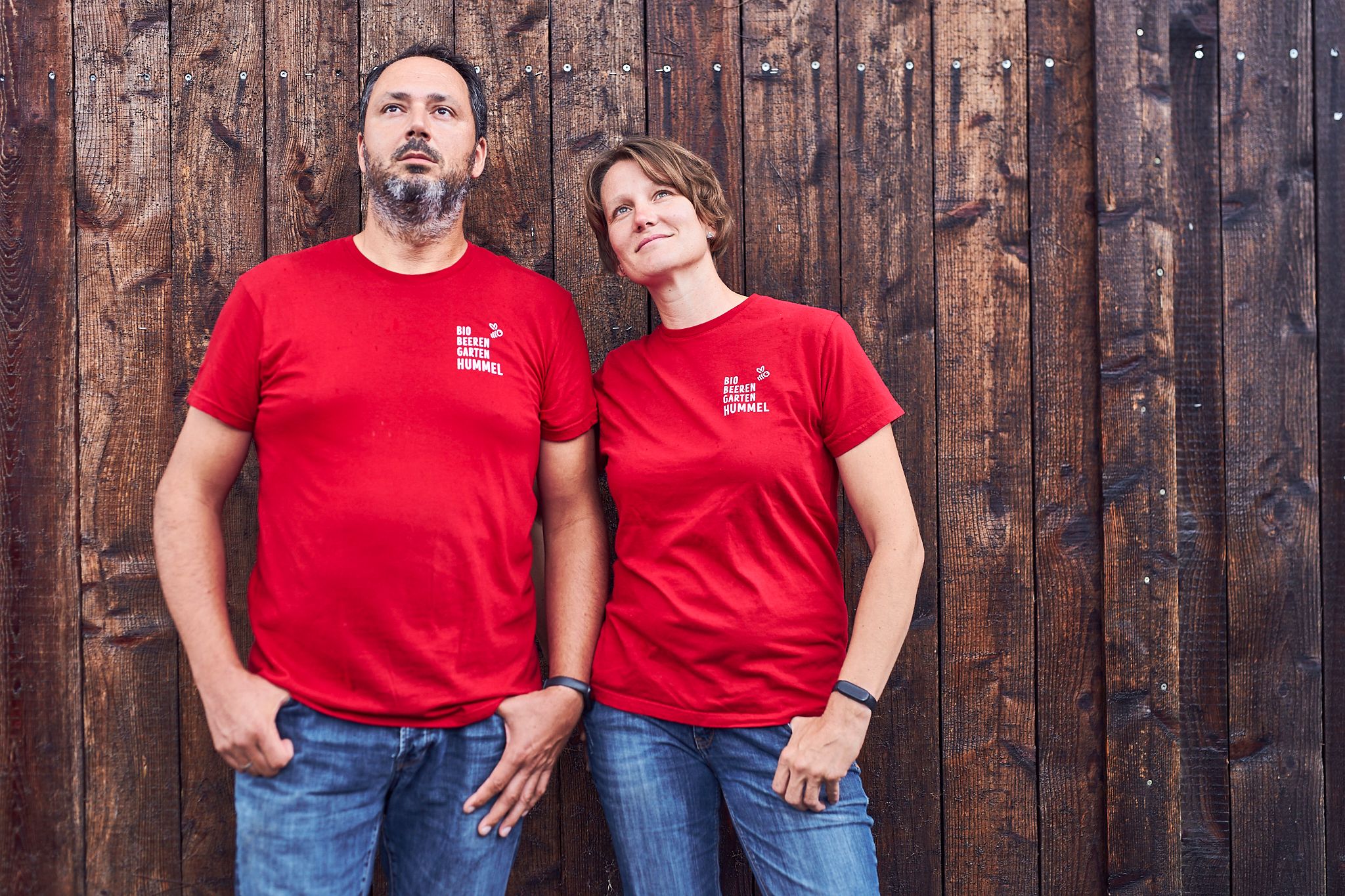 Zwei Personen in roten T-Shirts vor einer Holzwand.