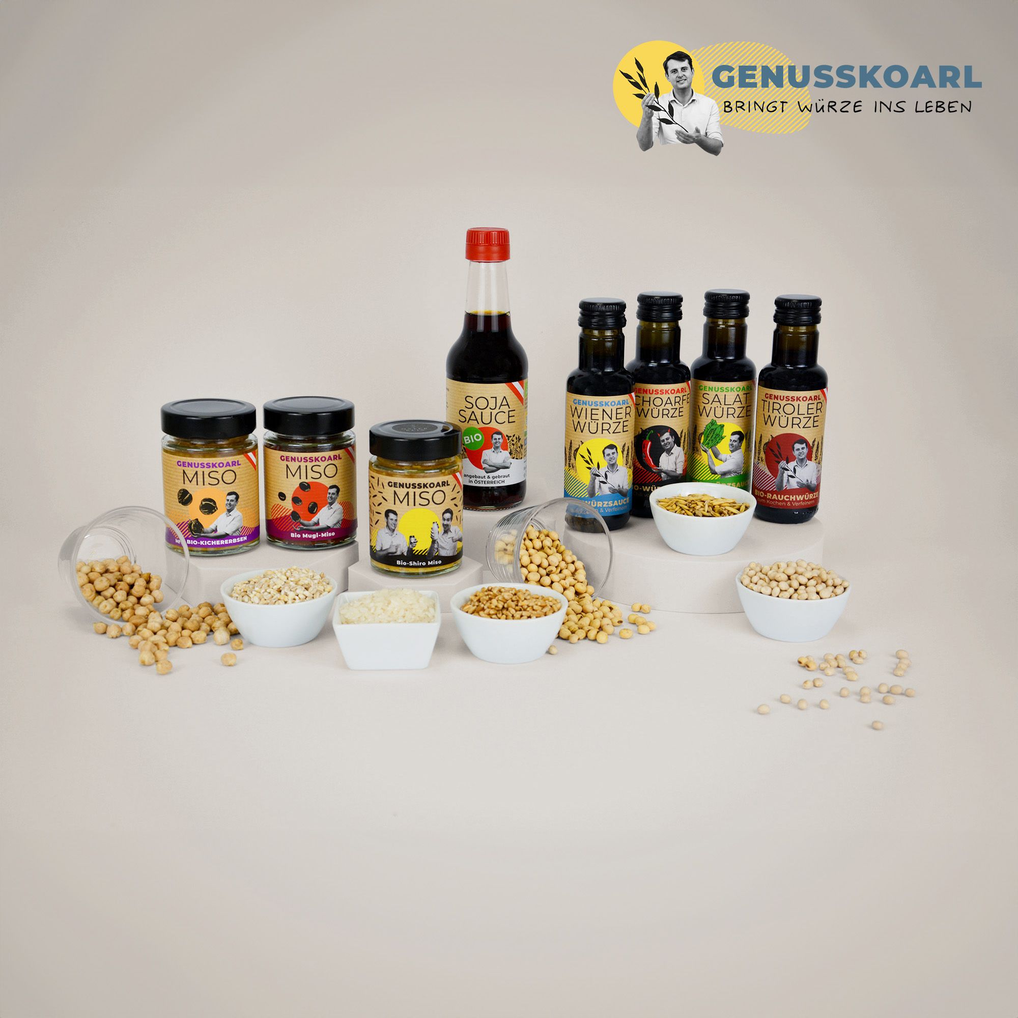 Verschiedene Genusskoarl Produkte, darunter Miso, Sojasauce und Würzöle, arrangiert mit Schalen voller Körner.
