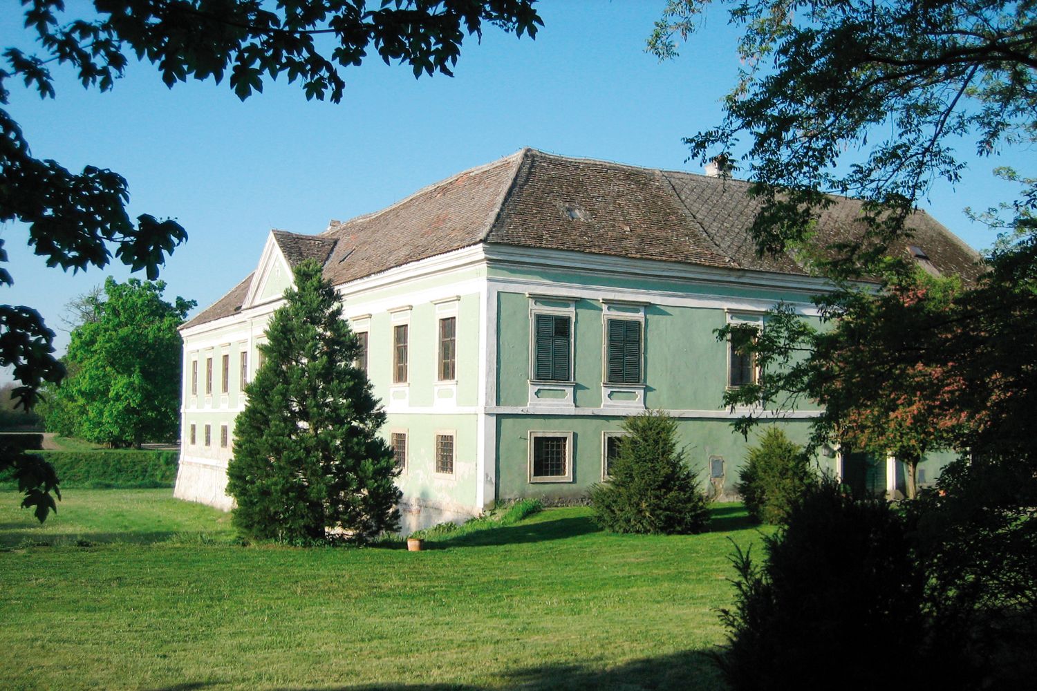 Ein altes Schloss mit grünem Anstrich und Ziegeldach, umgeben von Bäumen und Rasen.