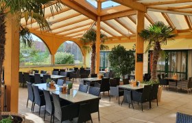 &Uuml;berdachte Terrasse eines Restaurants mit Palmen und Tischen.
