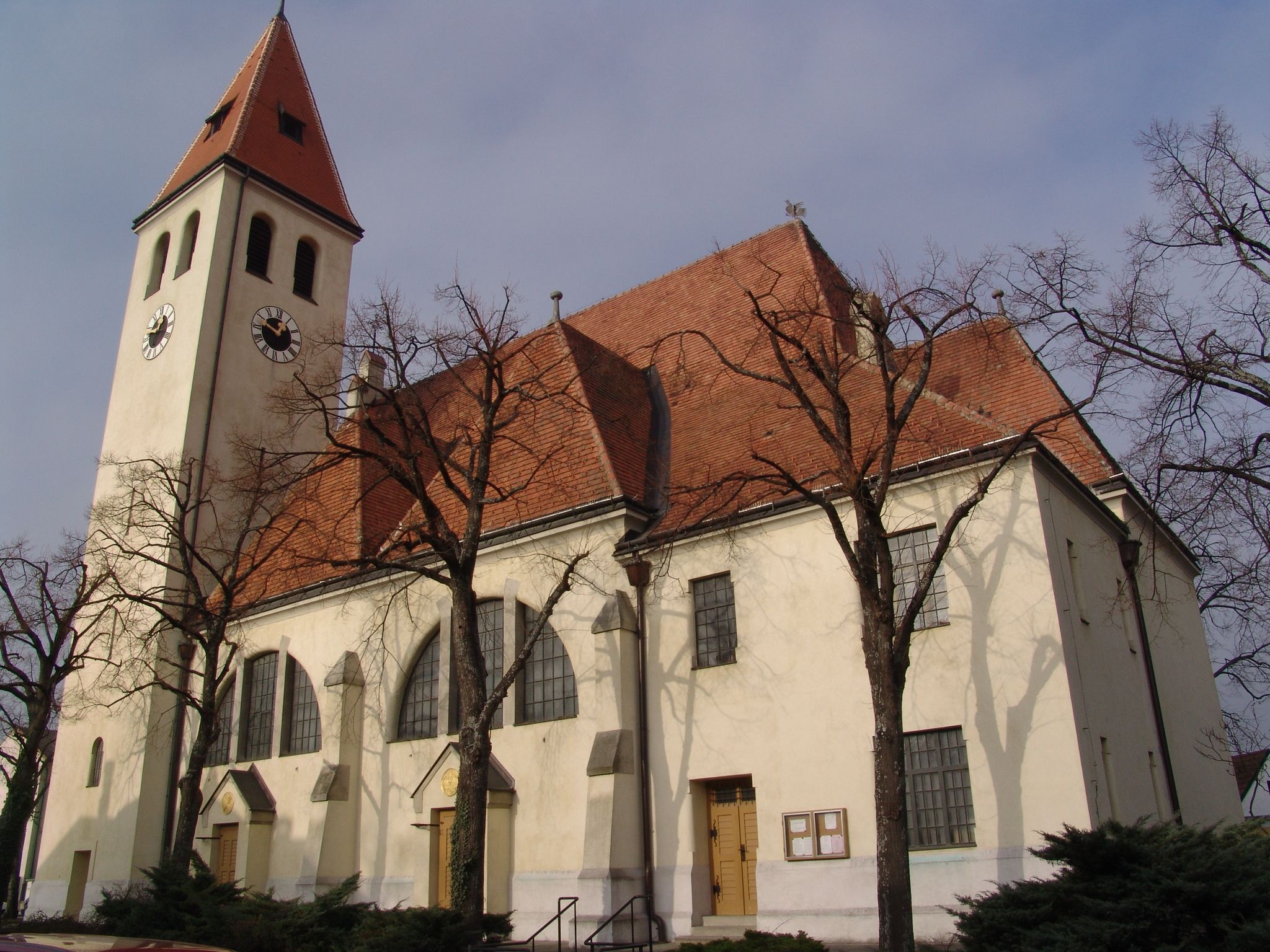 Kirche mit Turm und roten Ziegeldach, umgeben von kahlen Bäumen.