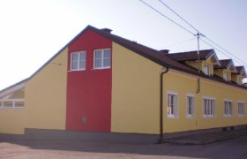 Außenansicht eines gelb-roten Gebäudes mit mehreren Fenstern und einem Satteldach.