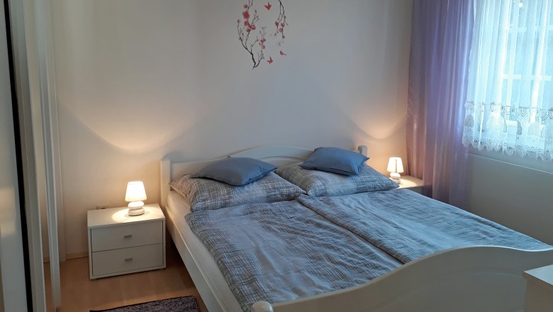 Ein gemütliches Schlafzimmer mit Doppelbett, zwei Nachttischen mit Lampen und lila Vorhängen.