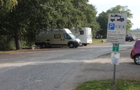 Wohnmobilstellplatz mit zwei geparkten Wohnmobilen und einem Hinweisschild.