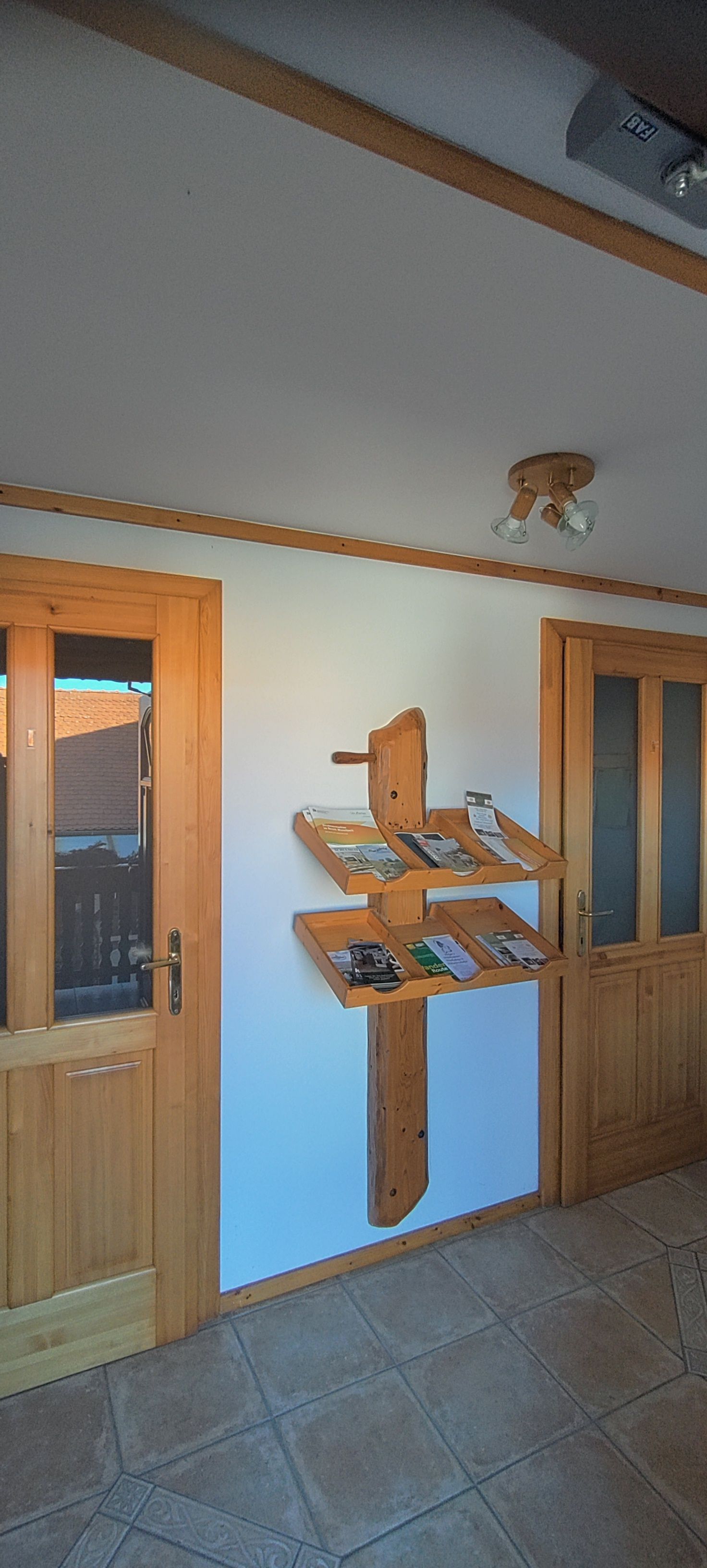 Ein Holzregal mit Prospekten an einer weißen Wand zwischen zwei Holztüren.