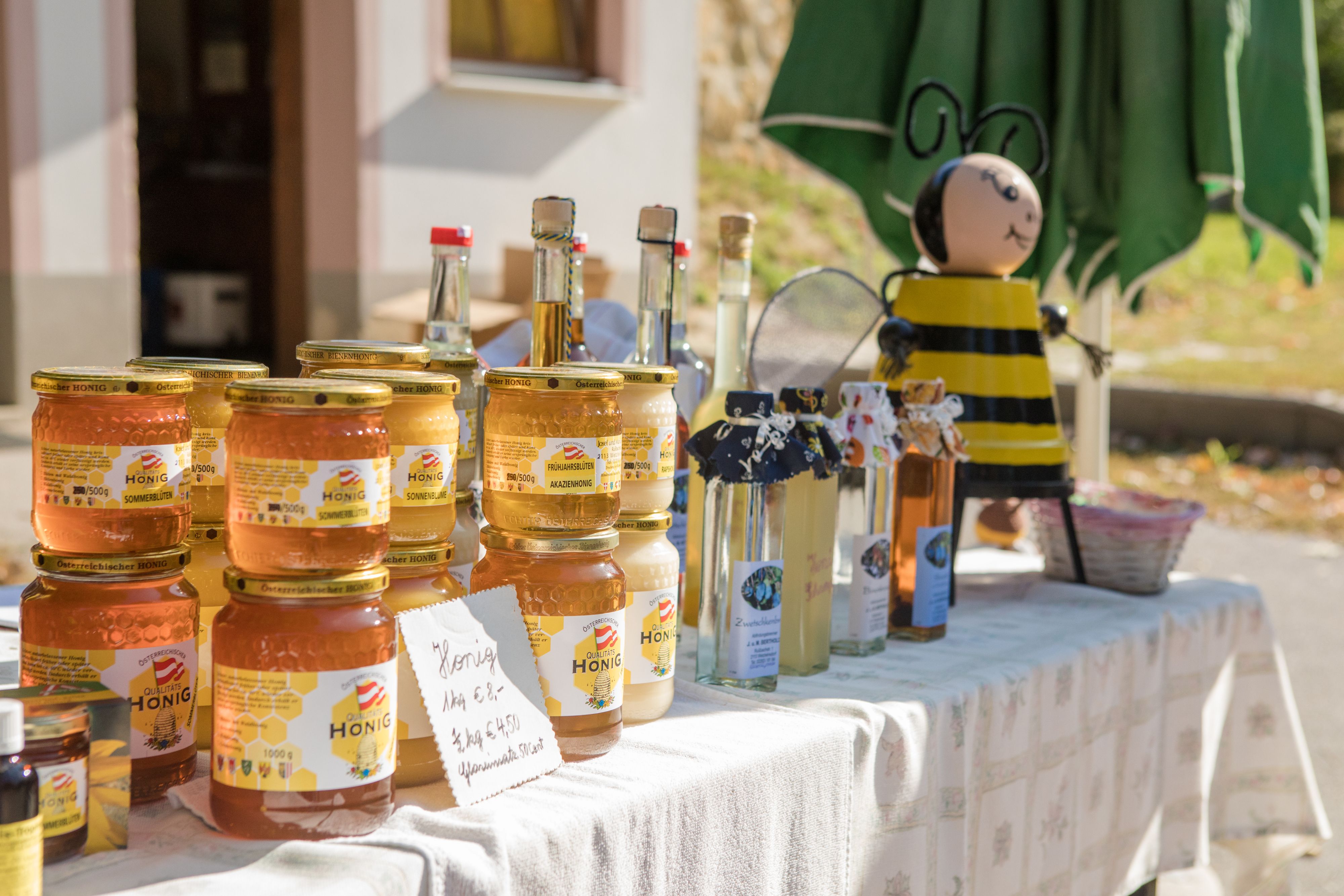 Honiggläser und Flaschen auf einem Tisch mit einer Bienenfigur im Hintergrund.