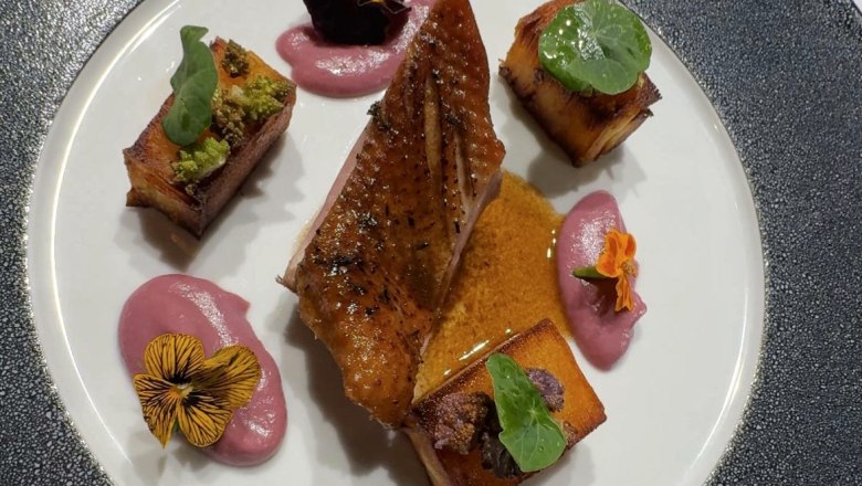 Gourmetgericht mit Entenbrust, Gem&uuml;sew&uuml;rfeln und Bl&uuml;ten auf einem eleganten Teller.