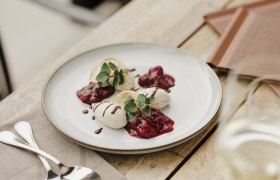 Ein Teller mit Mohnmousse, garniert mit Beerenkompott und Minzblättern, auf einem Holztisch.