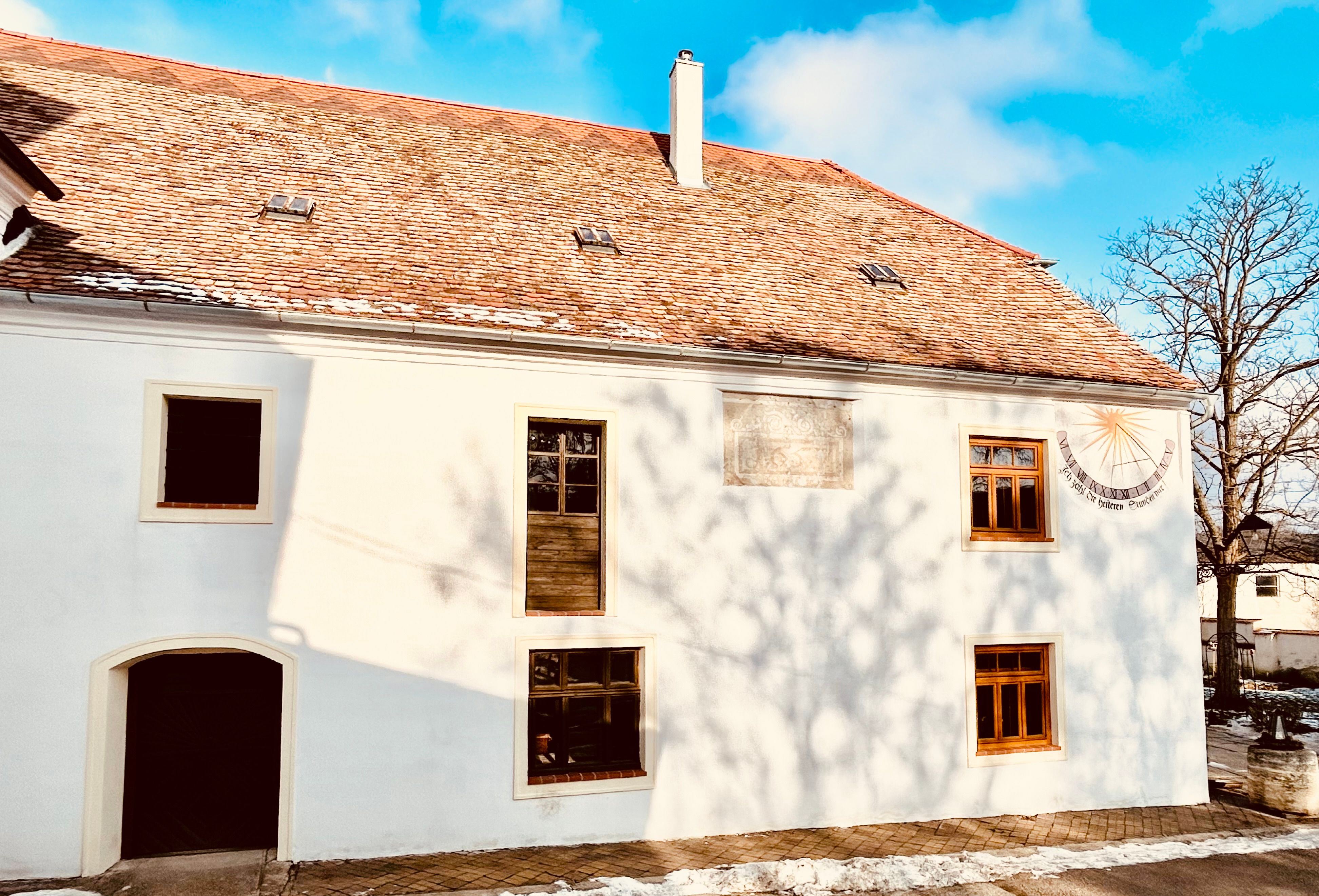 Ein altes Gebäude mit weißer Fassade und roten Ziegeln, das eine Sonnenuhr an der Wand hat.