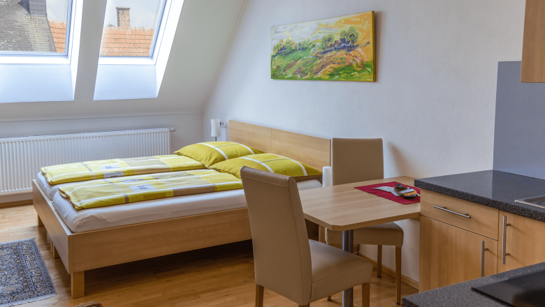 Doppelzimmer mit K&uuml;chenzeile, Bett, Tisch und St&uuml;hlen.