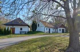 Wei&szlig;e Geb&auml;ude mit roten D&auml;chern in l&auml;ndlicher Umgebung, B&auml;ume im Vordergrund.